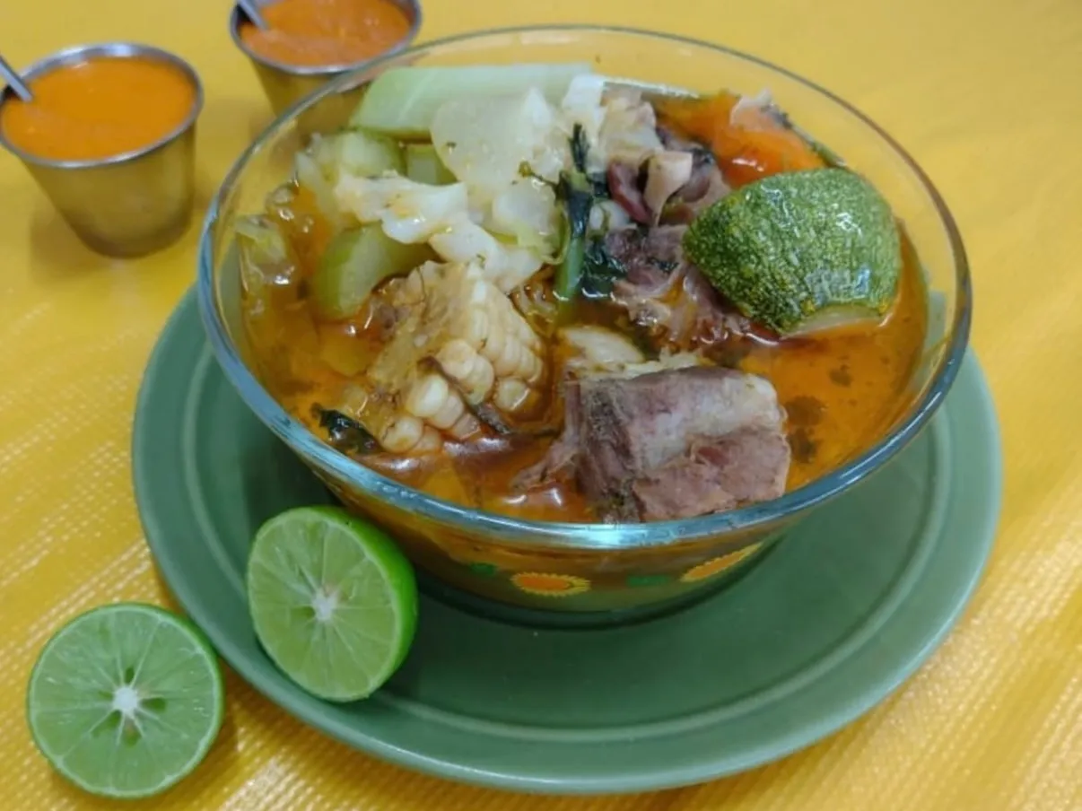 Caldo con carne de res, elote, calabaza y verduras, servido con limones