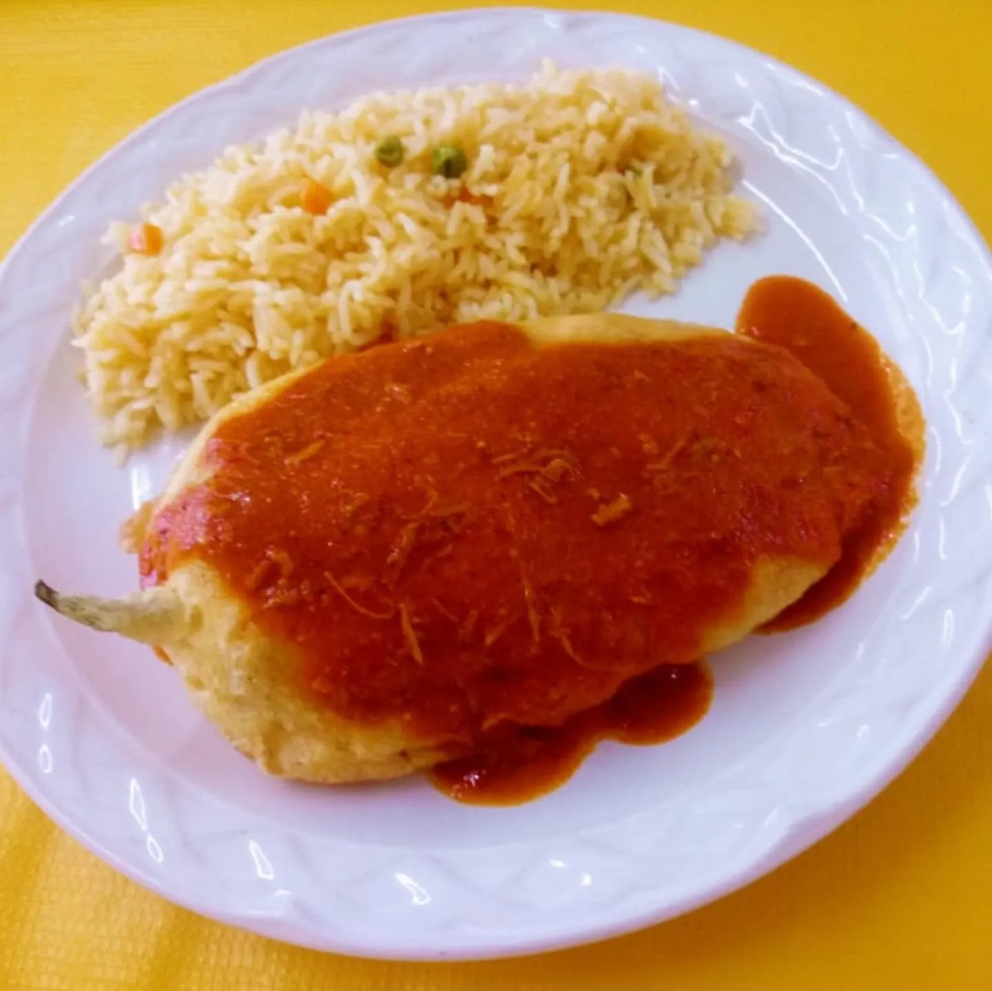 Chile poblano relleno bañado en salsa roja con arroz